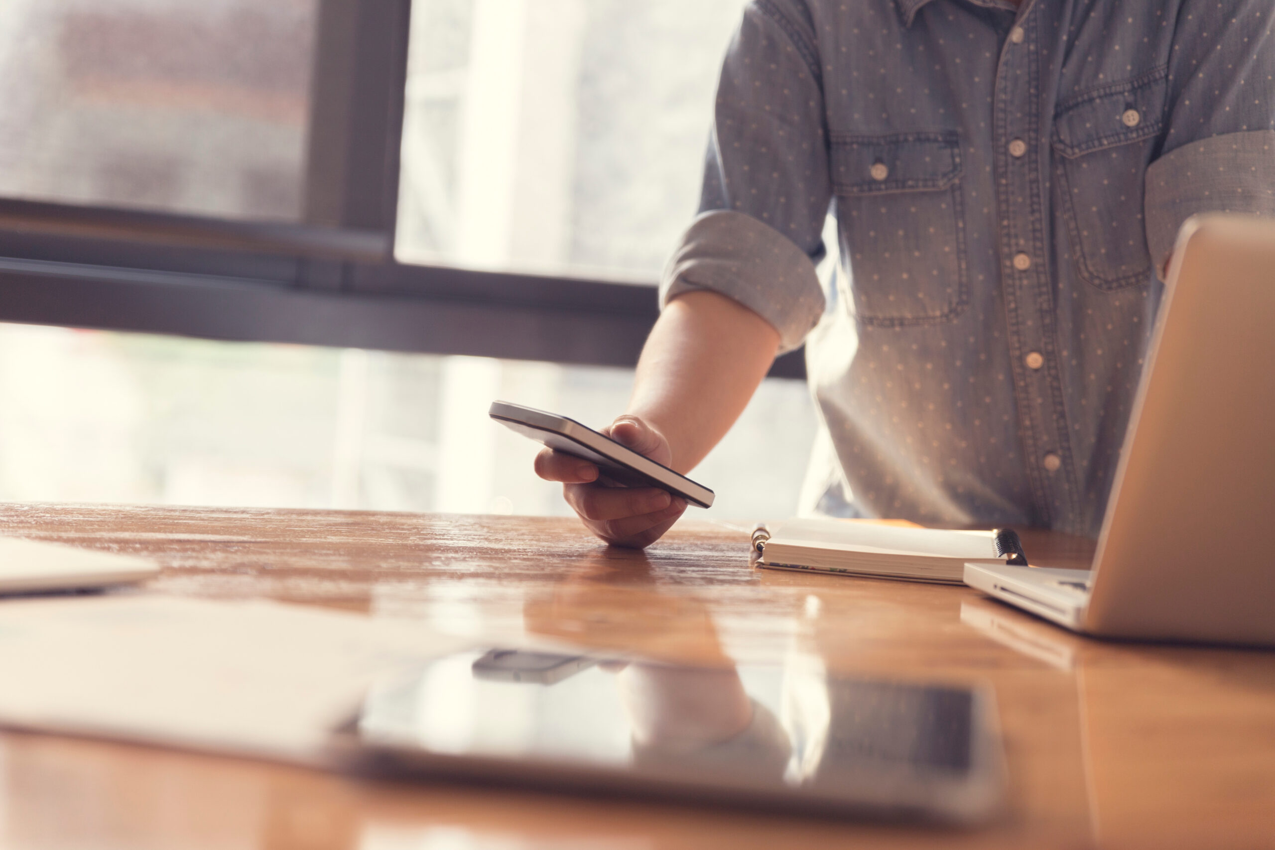 woman's hand holding smartphone with laptop computer for working concept, selective focus and vintage tone